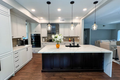 Large trendy laminate floor, brown floor and tray ceiling eat-in kitchen photo in San Diego with an undermount sink, shaker cabinets, white cabinets, quartz countertops, beige backsplash, porcelain backsplash, black appliances, an island and white countertops