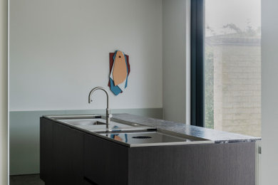 Mid-sized trendy galley marble floor and brown floor open concept kitchen photo in Other with an undermount sink, beaded inset cabinets, gray cabinets, stainless steel countertops, brown backsplash, marble backsplash, black appliances, an island and gray countertops