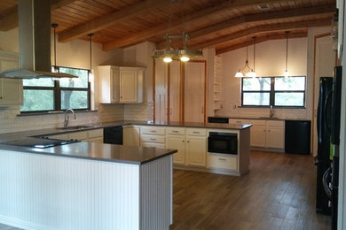Mid-sized cottage u-shaped medium tone wood floor and brown floor kitchen photo in Dallas with an undermount sink, raised-panel cabinets, white cabinets, solid surface countertops, white backsplash, black appliances, a peninsula and subway tile backsplash