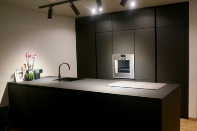 Mittelgroße Moderne Wohnküche mit Waschbecken, flächenbündigen Schrankfronten, schwarzen Schränken, Küchengeräten aus Edelstahl, hellem Holzboden, Halbinsel und schwarzer Arbeitsplatte in Nürnberg