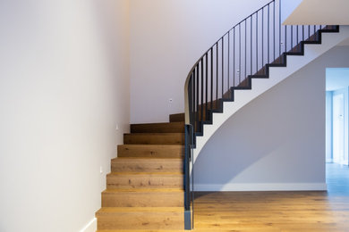Ejemplo de escalera curva actual grande con escalones de madera, contrahuellas de madera y barandilla de metal