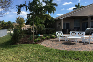 Mid-sized tropical backyard patio in Miami with natural stone pavers and a roof extension.