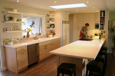 Example of a mid-sized trendy galley medium tone wood floor eat-in kitchen design in Vancouver with a double-bowl sink, flat-panel cabinets, light wood cabinets, solid surface countertops, beige backsplash, ceramic backsplash, stainless steel appliances and an island