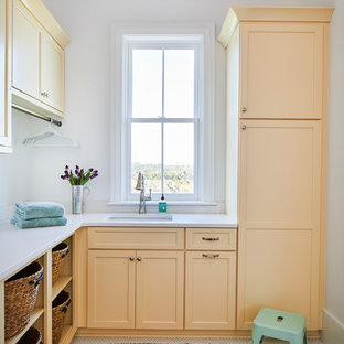 Photo of a beach style l-shaped separated utility room in Charleston with a submerged sink, engineered stone countertops, white walls, white floors, white worktops, shaker cabinets and orange cabinets.