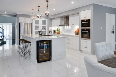 This is an example of a large modern l-shaped open plan kitchen in Brisbane with a drop-in sink, recessed-panel cabinets, white cabinets, quartz benchtops, white splashback, subway tile splashback, stainless steel appliances, porcelain floors, with island and white floor.