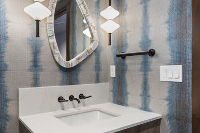 Example of a mid-sized trendy wallpaper powder room design in Other with flat-panel cabinets, brown cabinets, blue walls, an undermount sink, quartzite countertops, white countertops and a built-in vanity