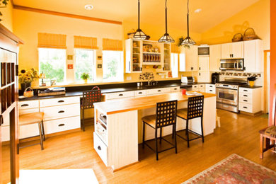 Eat-in kitchen - cottage l-shaped medium tone wood floor and brown floor eat-in kitchen idea in Los Angeles with a drop-in sink, recessed-panel cabinets, white cabinets, soapstone countertops, black backsplash, stone slab backsplash, stainless steel appliances, an island and black countertops