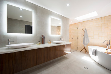 Photo of a large mediterranean master bathroom in Perth with dark wood cabinets, a freestanding tub, an alcove shower, a wall-mount toilet, multi-coloured tile, multi-coloured walls, porcelain floors, a vessel sink, solid surface benchtops, limestone, grey floor and a hinged shower door.