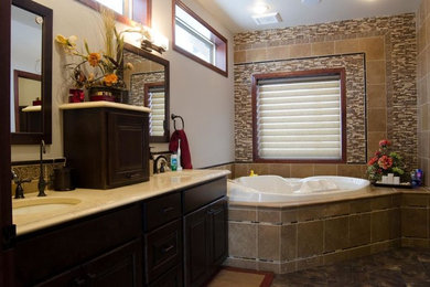 Mid-sized elegant master beige tile and matchstick tile travertine floor corner bathtub photo in Other with raised-panel cabinets, dark wood cabinets, white walls, an undermount sink and quartz countertops