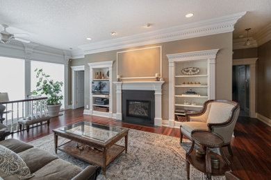 Example of a mid-sized classic open concept dark wood floor and brown floor living room design in Edmonton with beige walls, a standard fireplace, a stone fireplace and a media wall