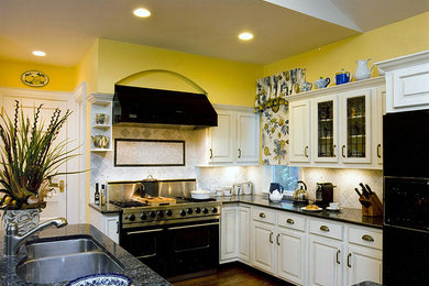 Example of a mid-sized country medium tone wood floor and brown floor enclosed kitchen design in Other with a drop-in sink, raised-panel cabinets, gray cabinets, granite countertops, gray backsplash, marble backsplash, black appliances, an island and blue countertops