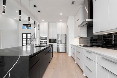 Large minimalist l-shaped light wood floor and beige floor open concept kitchen photo in Little Rock with an undermount sink, flat-panel cabinets, white cabinets, quartz countertops, black backsplash, glass tile backsplash, stainless steel appliances, an island and black countertops