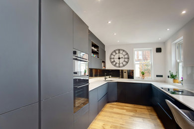 This is an example of a medium sized modern u-shaped open plan kitchen in Other with a single-bowl sink, flat-panel cabinets, black cabinets, quartz worktops, mirror splashback, black appliances and white worktops.