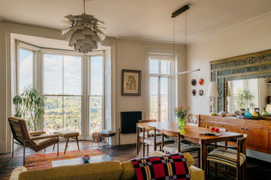 This is an example of a medium sized eclectic dining room in Sussex with white walls, dark hardwood flooring, a wood burning stove, a stone fireplace surround, brown floors and feature lighting.
