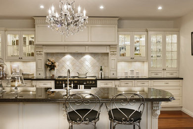 Mid-sized elegant medium tone wood floor and brown floor eat-in kitchen photo in New York with a farmhouse sink, glass-front cabinets, white cabinets, granite countertops, beige backsplash, stone tile backsplash, stainless steel appliances and an island