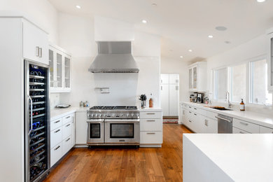 Open concept kitchen - large modern l-shaped medium tone wood floor open concept kitchen idea in Phoenix with an undermount sink, flat-panel cabinets, white cabinets, quartz countertops, white backsplash, porcelain backsplash, stainless steel appliances and a peninsula