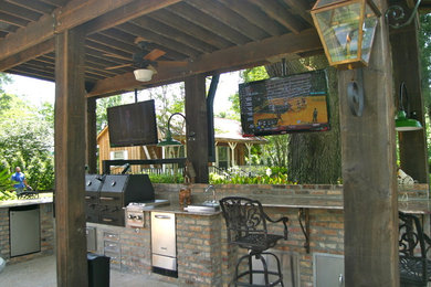 Large traditional backyard patio in New Orleans with an outdoor kitchen, a pergola and brick pavers.