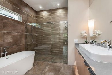 Design ideas for a mid-sized contemporary master bathroom in Orlando with flat-panel cabinets, light wood cabinets, a freestanding tub, a sliding shower screen, a curbless shower, brown tile, beige tile, brown walls, an integrated sink, a one-piece toilet, metal tile, ceramic floors, solid surface benchtops and beige floor.