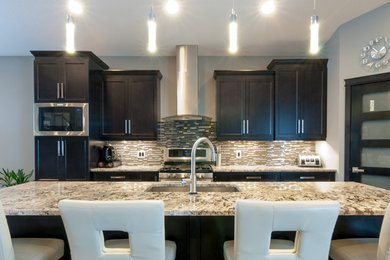 Example of a mid-sized trendy single-wall dark wood floor and brown floor open concept kitchen design in Other with an undermount sink, shaker cabinets, black cabinets, granite countertops, multicolored backsplash, glass sheet backsplash, stainless steel appliances and an island