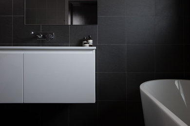 Inspiration for a mid-sized contemporary master bathroom in Sydney with flat-panel cabinets, white cabinets, a freestanding tub, an open shower, a one-piece toilet, black tile, ceramic tile, black walls, ceramic floors, an integrated sink, laminate benchtops, black floor and an open shower.