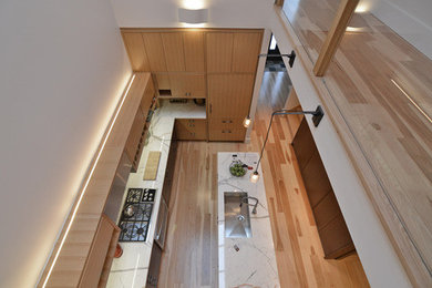 Example of a mid-sized minimalist single-wall light wood floor and beige floor eat-in kitchen design in Philadelphia with an undermount sink, flat-panel cabinets, beige cabinets, solid surface countertops, white backsplash, subway tile backsplash, stainless steel appliances, an island and white countertops