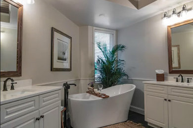 Photo of a large traditional ensuite bathroom in Minneapolis with shaker cabinets, white cabinets, a freestanding bath, a built-in shower, a one-piece toilet, beige tiles, ceramic tiles, beige walls, ceramic flooring, a submerged sink, engineered stone worktops, black floors, a hinged door, white worktops, a wall niche, double sinks, a built in vanity unit, a timber clad ceiling and wainscoting.