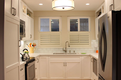 Photo of a small transitional u-shaped eat-in kitchen in Los Angeles with a double-bowl sink, shaker cabinets, white cabinets, solid surface benchtops, white splashback, subway tile splashback, stainless steel appliances, light hardwood floors, no island, beige floor and white benchtop.