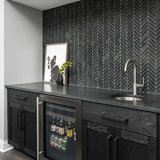 Inredning av en klassisk mellanstor svarta linjär svart hemmabar med vask, med en undermonterad diskho, svarta skåp, svart stänkskydd, mörkt trägolv, skåp i shakerstil, bänkskiva i täljsten och brunt golv