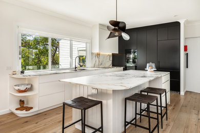 This is an example of a large contemporary l-shaped open plan kitchen in Sydney with an undermount sink, flat-panel cabinets, solid surface benchtops, porcelain splashback, black appliances, medium hardwood floors and with island.