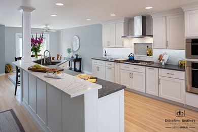 Large trendy single-wall light wood floor and beige floor eat-in kitchen photo in Providence with an undermount sink, recessed-panel cabinets, white cabinets, quartz countertops, white backsplash, porcelain backsplash, stainless steel appliances, an island and gray countertops