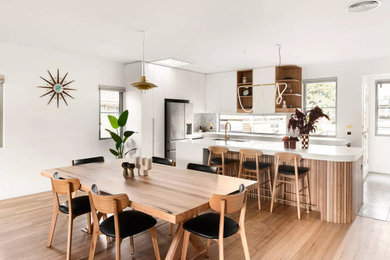 Inspiration for a mid-sized modern u-shaped light wood floor and brown floor eat-in kitchen remodel in Los Angeles with a drop-in sink, flat-panel cabinets, white cabinets, quartz countertops, gray backsplash, porcelain backsplash, stainless steel appliances, an island and white countertops