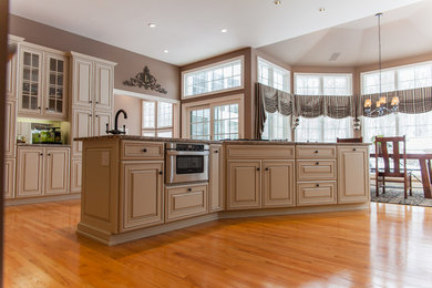 Huge elegant u-shaped light wood floor eat-in kitchen photo in New York with an undermount sink, raised-panel cabinets, beige cabinets, granite countertops, beige backsplash, terra-cotta backsplash, paneled appliances and an island