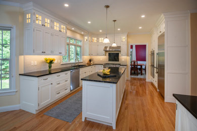 Mid-sized minimalist medium tone wood floor and brown floor eat-in kitchen photo in Boston with an undermount sink, shaker cabinets, white cabinets, quartzite countertops, white backsplash, ceramic backsplash, stainless steel appliances, an island and black countertops