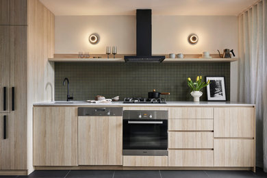 Small scandinavian single-wall open plan kitchen in Melbourne with an undermount sink, flat-panel cabinets, light wood cabinets, quartz benchtops, green splashback, ceramic splashback, black appliances, light hardwood floors, no island, yellow floor and grey benchtop.