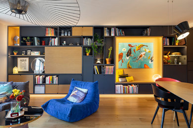 Photo of a large modern open concept family room in Paris with a library, white walls, light hardwood floors, a concealed tv and brown floor.