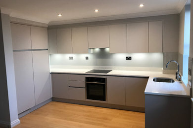 Photo of a medium sized contemporary u-shaped open plan kitchen in Sussex with a single-bowl sink, flat-panel cabinets, grey cabinets, quartz worktops, grey splashback, glass sheet splashback, integrated appliances, light hardwood flooring, no island and white worktops.
