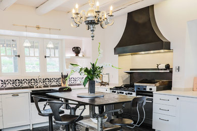 Example of a southwest l-shaped black floor kitchen design with a farmhouse sink, flat-panel cabinets, multicolored backsplash, black appliances, an island and white countertops