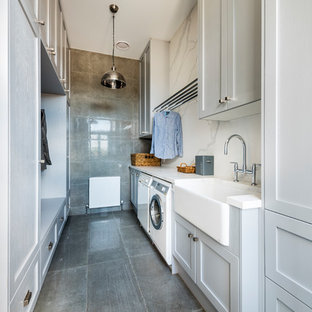 Photo of an expansive rural galley utility room in Melbourne with a belfast sink, shaker cabinets, grey cabinets, engineered stone countertops, concrete flooring, grey floors, white worktops, grey walls and a side by side washer and dryer.