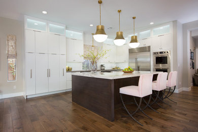This is an example of a large contemporary l-shaped eat-in kitchen in Las Vegas with flat-panel cabinets, white cabinets, white splashback, mosaic tile splashback, stainless steel appliances, medium hardwood floors, with island, brown floor, an undermount sink and multi-coloured benchtop.