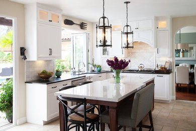 Inspiration for a mid-sized transitional u-shaped travertine floor kitchen remodel in San Diego with a farmhouse sink, recessed-panel cabinets, white cabinets, soapstone countertops, white backsplash, stone tile backsplash, stainless steel appliances and an island
