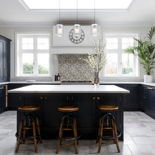 Design ideas for a large transitional u-shaped kitchen in Surrey with a farmhouse sink, blue cabinets, stainless steel appliances, with island, grey floor, white benchtop, shaker cabinets, beige splashback and mosaic tile splashback.
