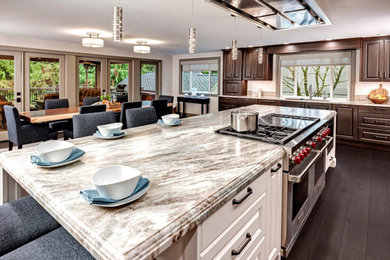 This is an example of an expansive transitional l-shaped open plan kitchen in Seattle with an undermount sink, raised-panel cabinets, brown cabinets, quartzite benchtops, beige splashback, porcelain splashback, stainless steel appliances, medium hardwood floors, with island, brown floor and multi-coloured benchtop.
