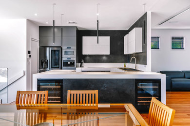 Inspiration for a contemporary u-shaped kitchen in Sunshine Coast with a drop-in sink, black appliances, medium hardwood floors, white benchtop, white cabinets, white splashback, porcelain splashback and with island.