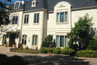 This is an example of a large transitional three-storey stucco beige house exterior in Dallas with a shingle roof.
