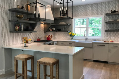Mid-sized cottage u-shaped light wood floor and beige floor eat-in kitchen photo with a farmhouse sink, flat-panel cabinets, gray cabinets, quartz countertops, white backsplash, ceramic backsplash, paneled appliances and a peninsula