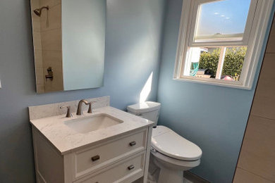 Inspiration for a mid-sized gray tile and porcelain tile porcelain tile, gray floor and single-sink bathroom remodel in Los Angeles with open cabinets, white cabinets, a two-piece toilet, blue walls, an undermount sink, quartzite countertops, white countertops, a niche and a freestanding vanity