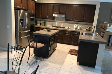 Example of a mid-sized minimalist u-shaped ceramic tile and gray floor open concept kitchen design in Orange County with an undermount sink, raised-panel cabinets, brown cabinets, quartz countertops, beige backsplash, stainless steel appliances and an island