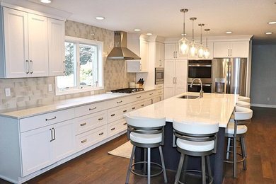 Example of a large transitional l-shaped medium tone wood floor and brown floor kitchen pantry design in Cedar Rapids with an undermount sink, recessed-panel cabinets, white cabinets, quartzite countertops, gray backsplash, porcelain backsplash, stainless steel appliances, an island and white countertops