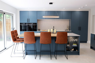 Inspiration for a large modern open plan kitchen in West Midlands with a single-bowl sink, flat-panel cabinets, blue cabinets, quartz worktops, white splashback, engineered quartz splashback, black appliances, porcelain flooring, an island, beige floors, white worktops and a feature wall.