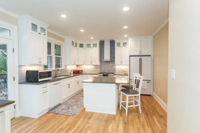 Example of a large transitional l-shaped light wood floor eat-in kitchen design in Atlanta with an undermount sink, shaker cabinets, white cabinets, quartzite countertops, gray backsplash, ceramic backsplash, white appliances, an island and gray countertops